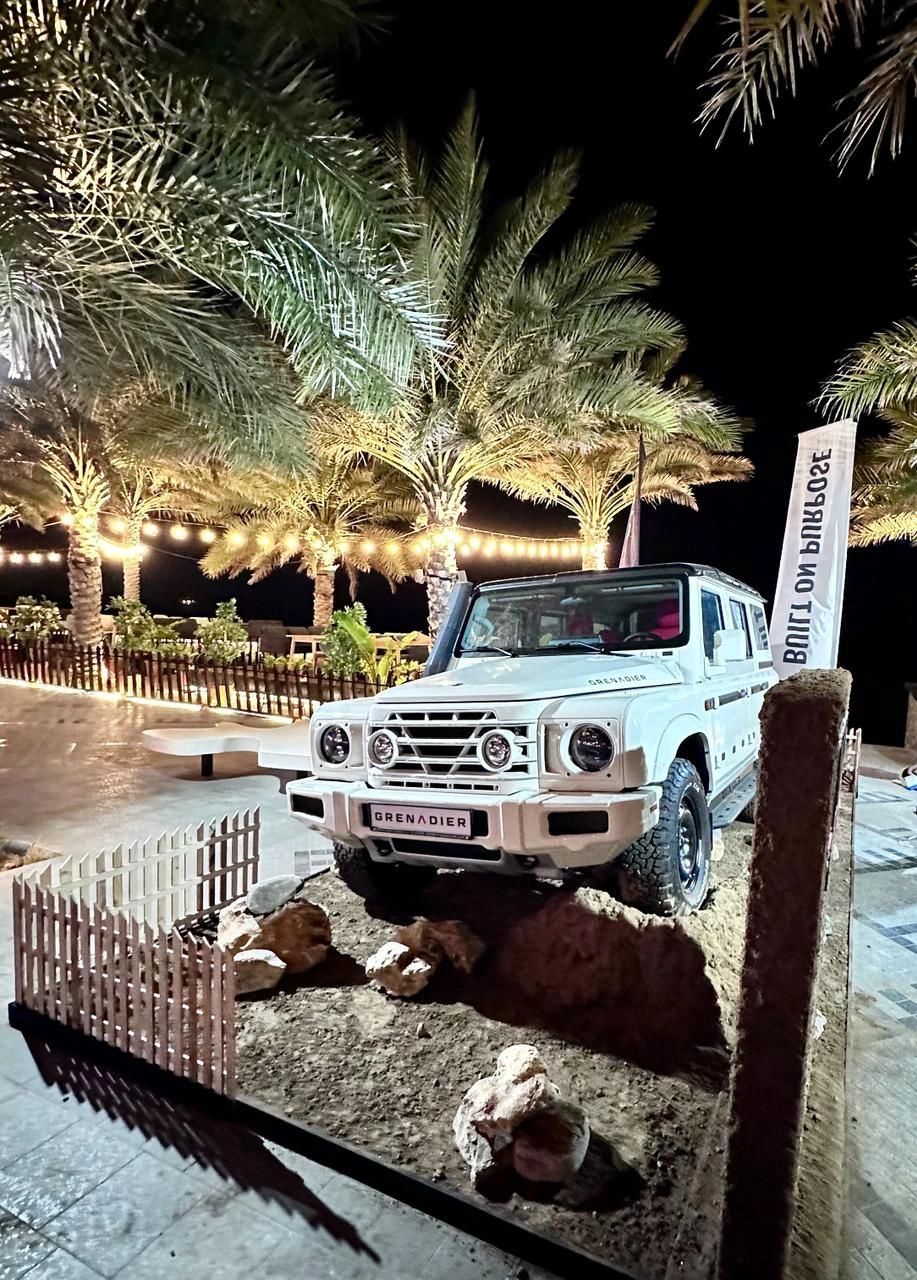 Front view of a white INEOS Grenadier displayed among rocks and textured ground at night